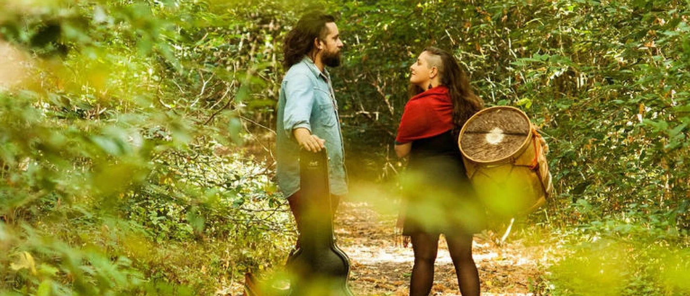 Duo Turica Doncel.jpg Zwei Musiker mit Gitarrenkoffer und Trommel, die sich auf einem Waldweg anschauen.