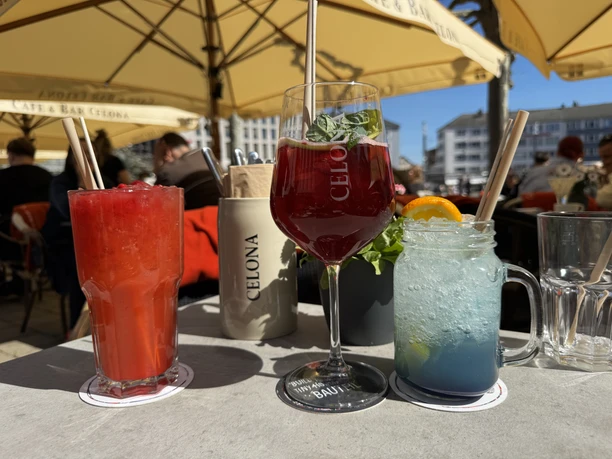 Im Außenbereich stehen drei Getränke auf einem Tisch. Zwei Cocktailgläser und ein Weinglas.