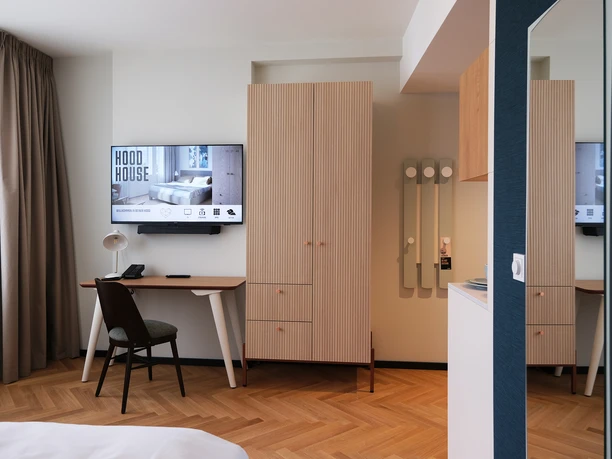 Hood House_HHKS_Space_Bedroom Ein Zimmer im Hood House mit dem Blick auf einen kleinen Schreibtisch, Fernseher und den Kleiderschrank.
