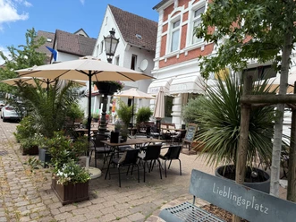 Außenterrasse des Lavanta Cafés mit Tischen, Sonnenschirmen und Pflanzen vor einem Backsteinhaus.