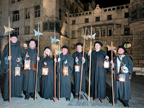 Les guides touristiques déguisés en veilleurs de nuit Bremme se tiennent dans l'obscurité devant le nouvel hôtel de ville de Leipzig, munis d'une lanterne.
