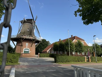 Hahnentanger Mühle.JPG Windmühle neben einem langgestreckten Backsteingebäude unter blauem Himmel