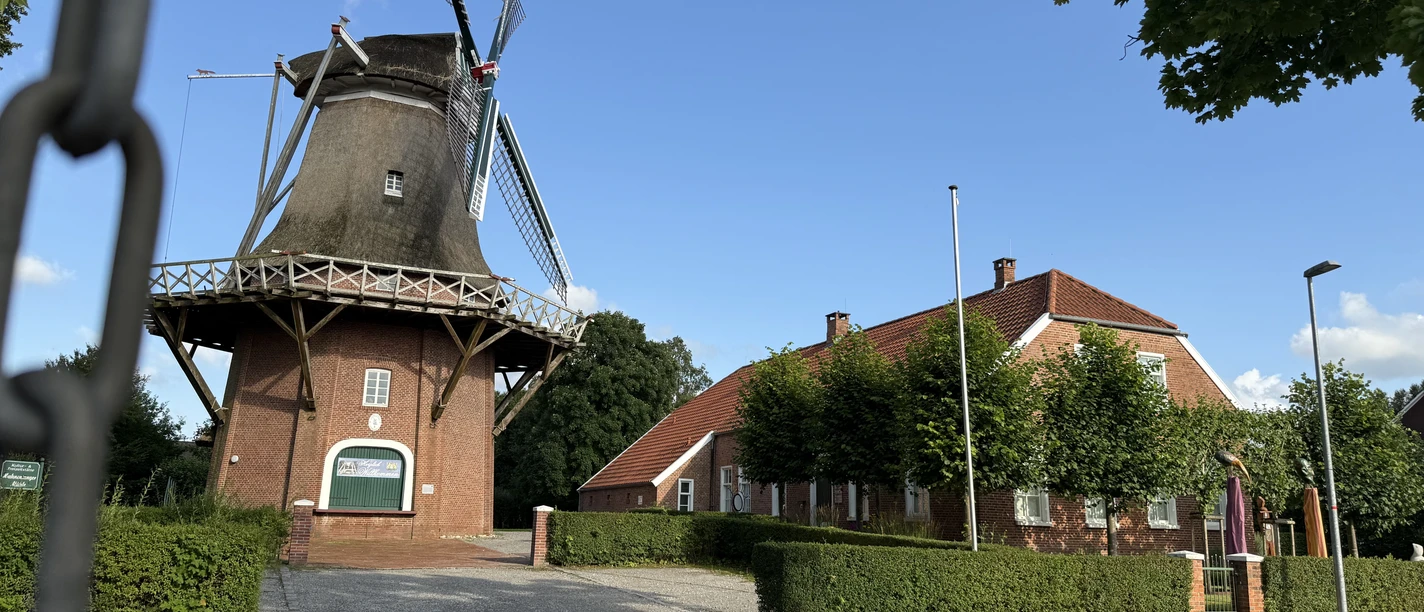 Hahnentanger Mühle.JPG Windmühle neben einem langgestreckten Backsteingebäude unter blauem Himmel