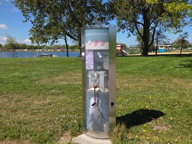 Münzautomat Souvenirmedaillen-Automat mit Otter-Motiv auf sonniger Wiese am Wasser.