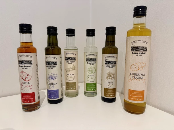 Six bottles of Leman Feinkost, containing various types of vinegar, oil, and dressing, lined up side by side.