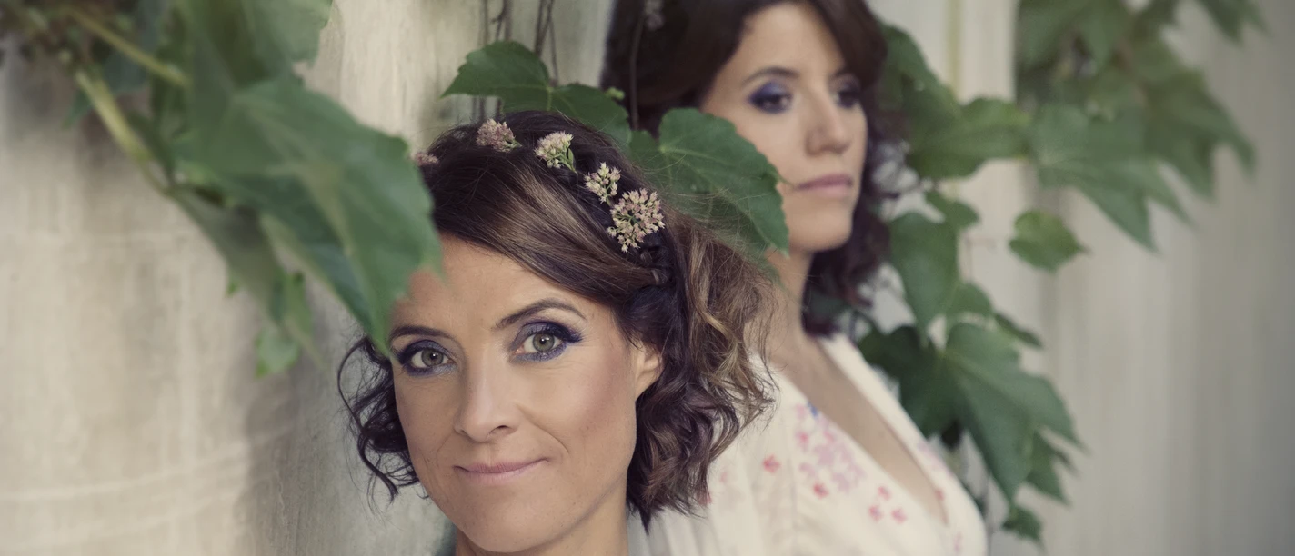 FJARILL_Midsommar_Foto_1_von_Anne_de_Wolf.jpg Die zwei Musikerinnen von Fjarill an einer begrünten Wand, eine trägt Blumen im Haar.