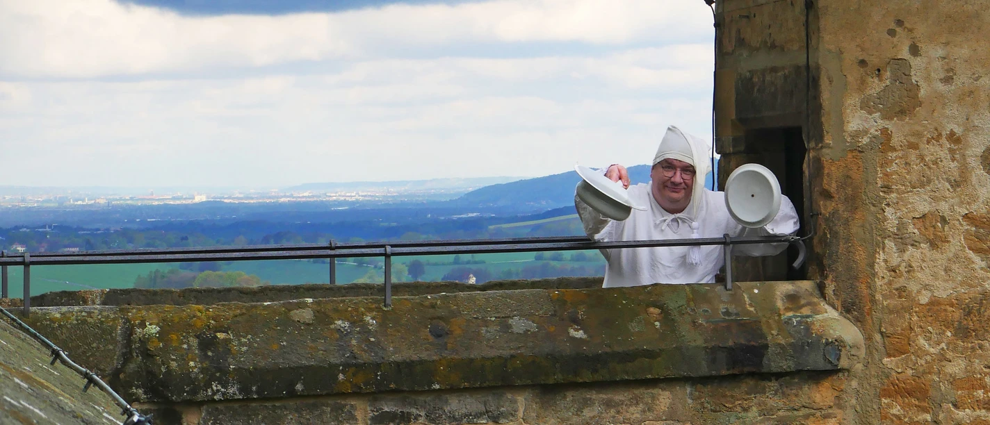 festung-anruechig.jpg Ein Mann in langem Nachthemd und mit Zipfelmütze mit Nachttopf an einem Wachturm der Festung Königstein