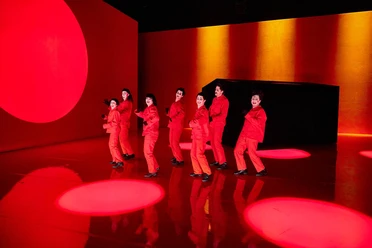 Rabatz! Eight people in red costumes dance on a stage in front of bright red lights