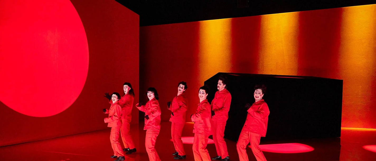 Rabatz! Eight people in red costumes dance on a stage in front of bright red lights