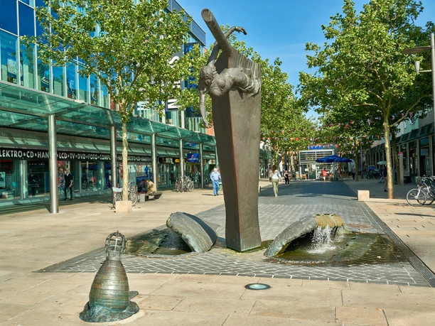 Stadtansichten von Bremerhaven Bronzebrunnen Bugwelle in Form eines Schiffsbugs mit Galionsfigur in einer Fußgängerzone.