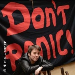 Person lehnt vor schwarzem Banner mit großem roten Schriftzug Don’t Panic!