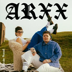 Zwei Personen sitzen entspannt auf Möbeln im Gras vor einem Erdwall mit ARXX-Schriftzug.