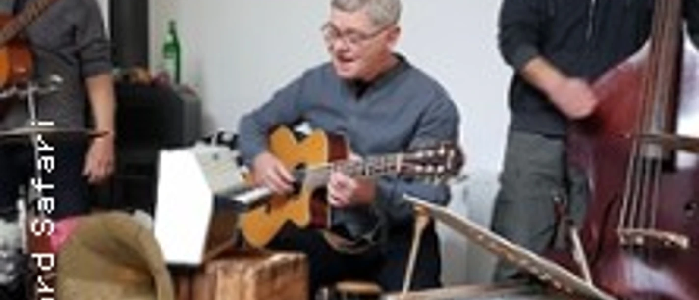 Mehrere Musiker spielen Akustikgitarre und Kontrabass in einem kleinen Innenraum.