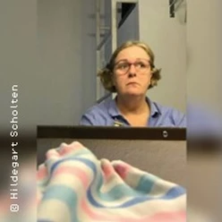 Eine Person mit Brille sitzt vor einem Tisch, im Vordergrund liegt ein bunt gestreiftes Tuch.