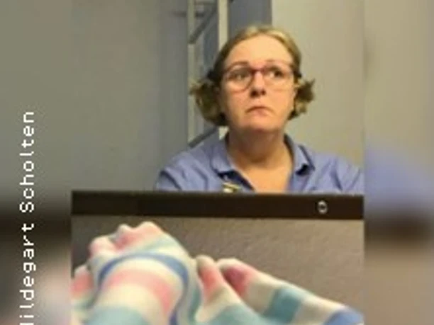 Eine Person mit Brille sitzt vor einem Tisch, im Vordergrund liegt ein bunt gestreiftes Tuch.