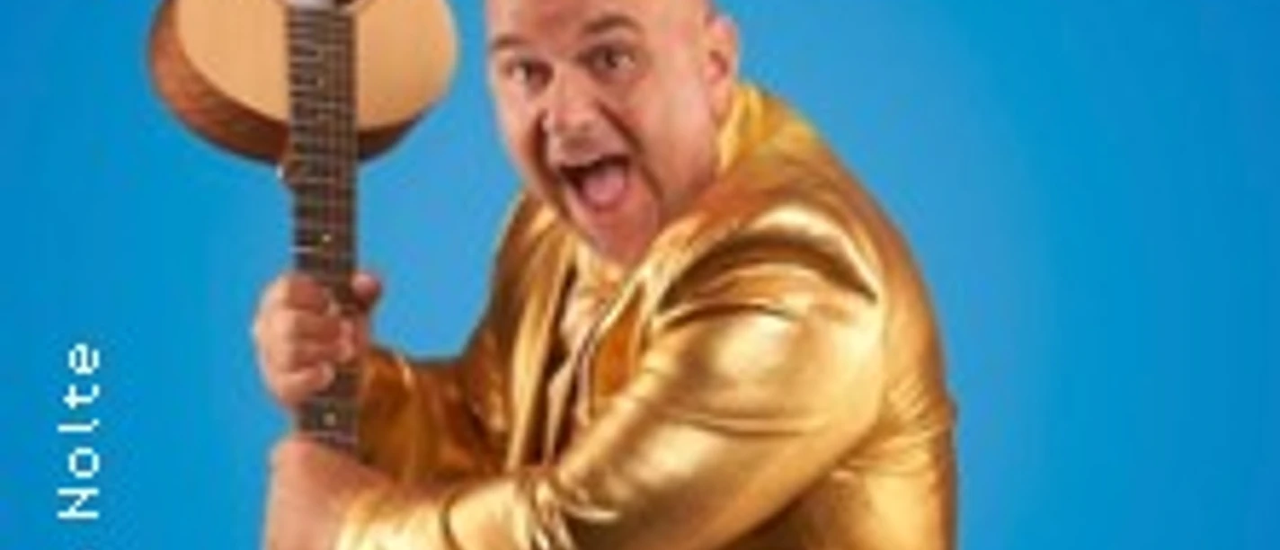 Ein Mann im goldenen Anzug hält eine Gitarre vor blauem Hintergrund und wirkt energiegeladen.