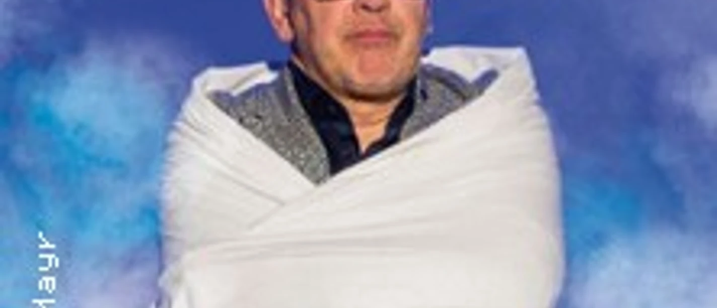 Eine Person steht auf einer Bühne und ist in ein helles Tuch gehüllt, umgeben von Nebel.