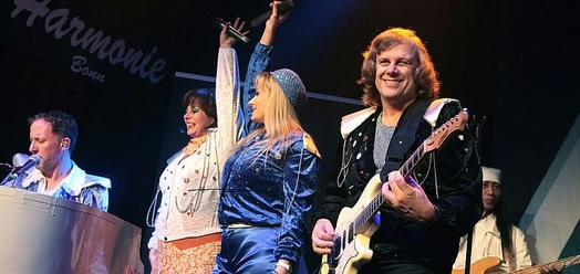 ABBA-Tribute-Band mit Sängerinnen, Gitarrist, Pianist und Schlagzeuger auf der Bühne