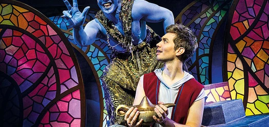 Aladin mit Wunderlampe und blauem Dschinni vor buntem Bühnenbild