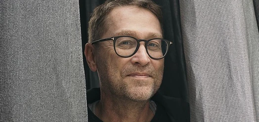 Porträt von Jan Weiler mit Brille zwischen grauen Vorhängen