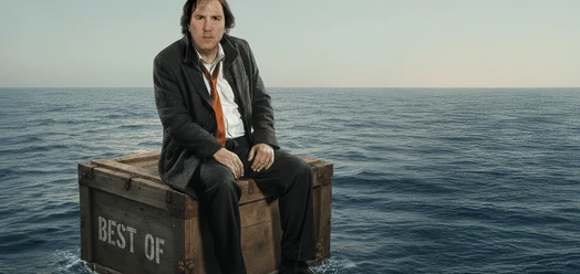 Stefan Waghubinger sitzt auf einer Holzkiste im Meer vor weitem Horizont