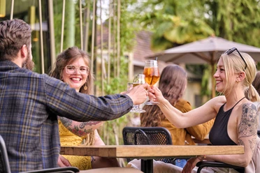 Café Siebenbergen auf der Blumeninsel Drei Personen sitzen draußen an einem Tisch und stoßen an.