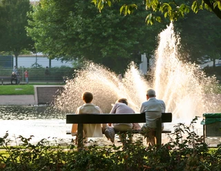 Springbrunnen am Holzhafen IMG_0834_WEB (c) Helmut Gross.jpg Drei Menschen auf einer Bank betrachten einen sprühenden Springbrunnen im Wasser.