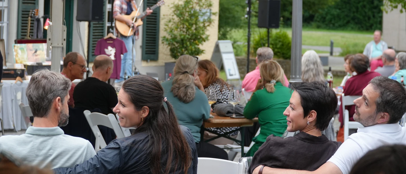 SE Saitenklänge Robert Carl Blank Bild Robert Scheuermeyer 260625 (21).JPG Open-Air‑Konzert mit Gitarrist auf kleiner Bühne und entspanntem Publikum an Tischen.