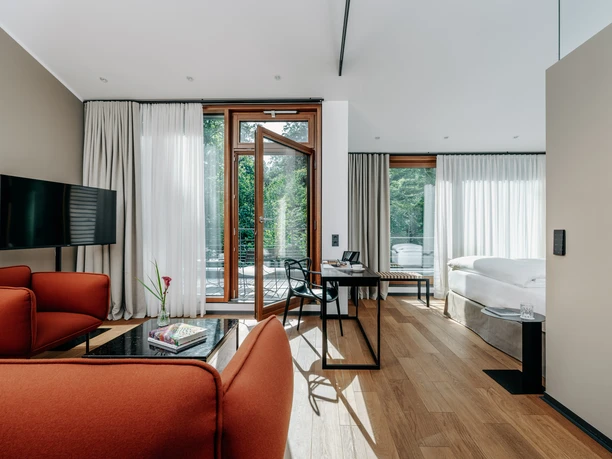 Diepeschrather Mühle Juniorsuite Helle Juniorsuite mit roten Sesseln, großem Bett, Holzboden und bodentiefen Fenstern.