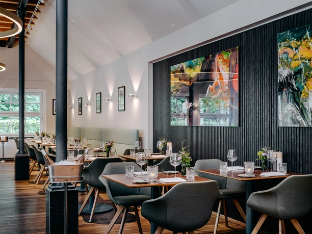 Brasserie Müllers in der Mühle Modernes Restaurant mit gedeckten Holztischen, grünen Stühlen und großer abstrakter Wandkunst.