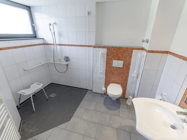 Badezimmer barrierearm Barrierearmes Bad mit ebener Dusche, Duschsitz, Haltegriffen und wandhängendem WC.