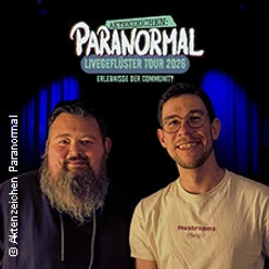 Zwei lächelnde Personen vor beleuchteter Bühne mit Logo der Paranormal Livegeflüster Tour.