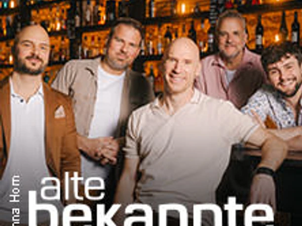 Fünf Männer stehen entspannt vor einer beleuchteten Regalwand mit Flaschen in einer Bar.