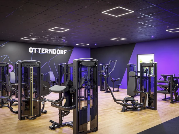 FITOMAT Otterndorf Kraft Moderner Fitnessbereich in Otterndorf: Schwarze Kraftgeräte vor einer stylischen lila Wand.