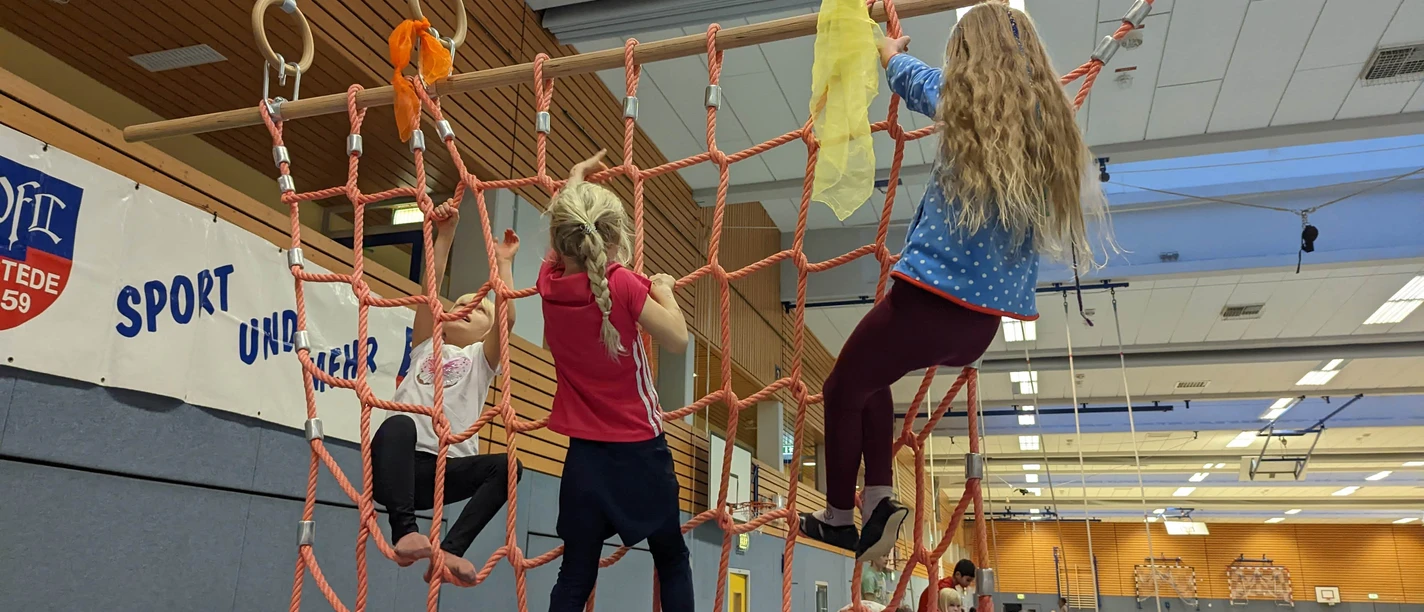 ActionTime2022 (374).jpg Kinder klettern auf einem großen Seilnetz, das in einer Turnhalle bei einer Veranstaltung hängt.