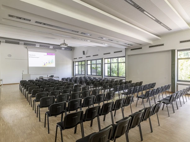 Tagungsraum Parlamentarisch Large, bright conference room with many rows of chairs, screen and wide windows overlooking the greenery