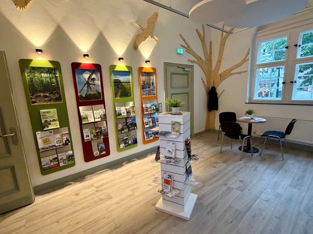 Tourist-Information (3).jpg Heller Raum der Tourist-Information mit bunten Prospektregalen, Infoständer und Sitzecke.
