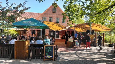 Spargeldiele mit Biergarten Außenterrasse mit Gästen vor Backsteingebäude, Schild wirbt für Spargelbuffet.