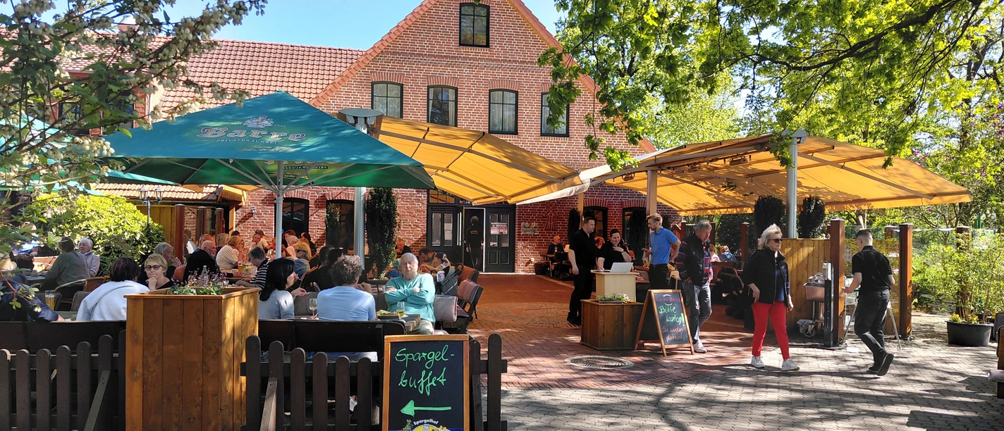 Spargeldiele mit Biergarten Außenterrasse mit Gästen vor Backsteingebäude, Schild wirbt für Spargelbuffet.