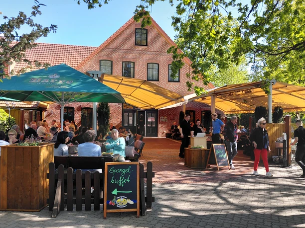 Spargeldiele mit Biergarten Außenterrasse mit Gästen vor Backsteingebäude, Schild wirbt für Spargelbuffet.