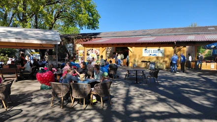 Hofladen & Eiscafé Außenterrasse am Spargelhof mit Gästen vor Hofladen und großer Erdbeerfigur