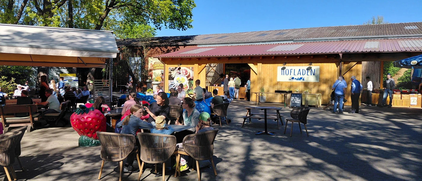 Hofladen & Eiscafé Außenterrasse am Spargelhof mit Gästen vor Hofladen und großer Erdbeerfigur