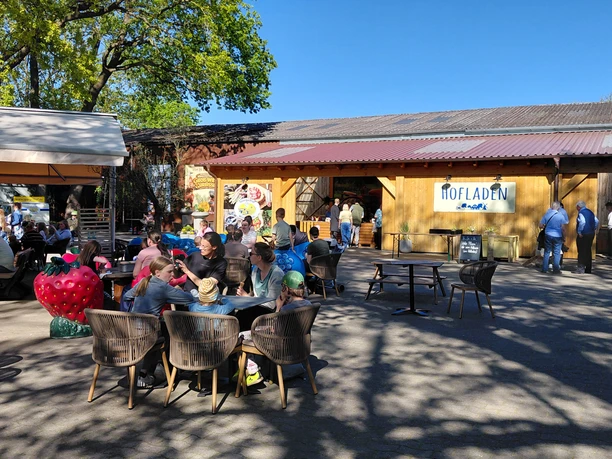 Hofladen & Eiscafé Außenterrasse am Spargelhof mit Gästen vor Hofladen und großer Erdbeerfigur