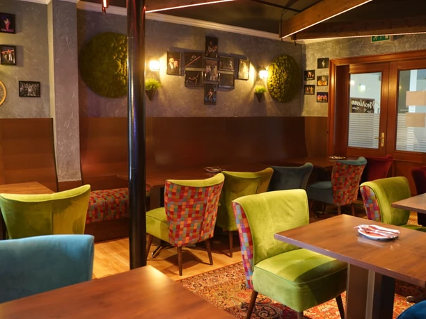 DSC02913 (c) Claudia Schulenberg_Erlebnis Bremerhaven_WEB.jpg Bunte Polstersessel und Holztische im warm beleuchteten Innenraum eines Restaurants.