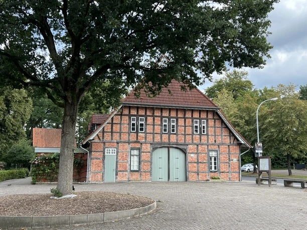 Lintler Krug (1).JPG Rotes Fachwerkhaus mit großem, grünem Holztor und Ziegeldach, davor ein großer Laubbaum.