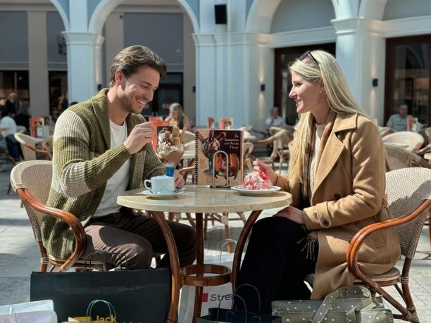 MOB_shoppingerlebnis_5_Bildrechte Mira Züchner_Mehrwert_KI optimiert_800x600.jpg Lachendes Paar mit Einkaufstaschen genießt Eis und Kaffee am Tisch im Outlet.