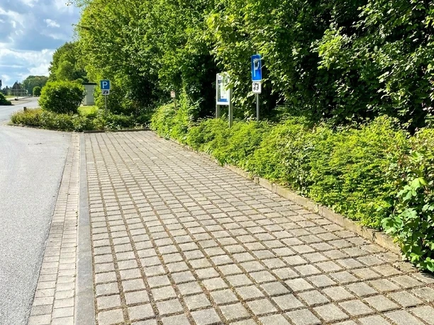 Wohnmobilstellplatz Am Cronsbach, Steinhagen - Stellplatz (C) Gemeinde Steinhagen.jpg Befestigter Wohnmobilstellplatz mit zwei Parkflächen am Straßenrand, umgeben von Bäumen und Hecken