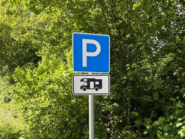 Wohnmobilstellplatz Am Cronsbach, Steinhagen - Parken (C) Gemeinde Steinhagen.jpeg Parkplatzschild für Wohnmobile am Cronsbach in Steinhagen vor grünen Bäumen