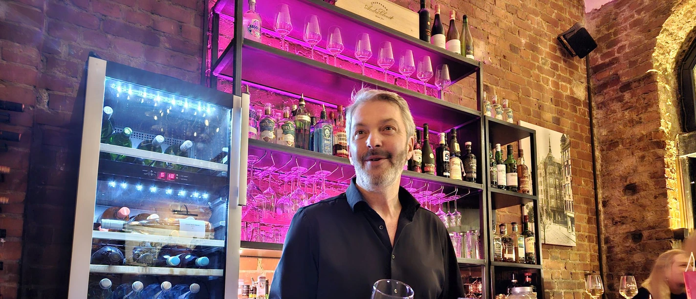 20240222_202618 (c) Tanja Mehl_Erlebnis Bremerhaven_WEB.jpg Freundlicher Barkeeper am Tresen vor Backsteinwand mit pink beleuchtetem Regal.