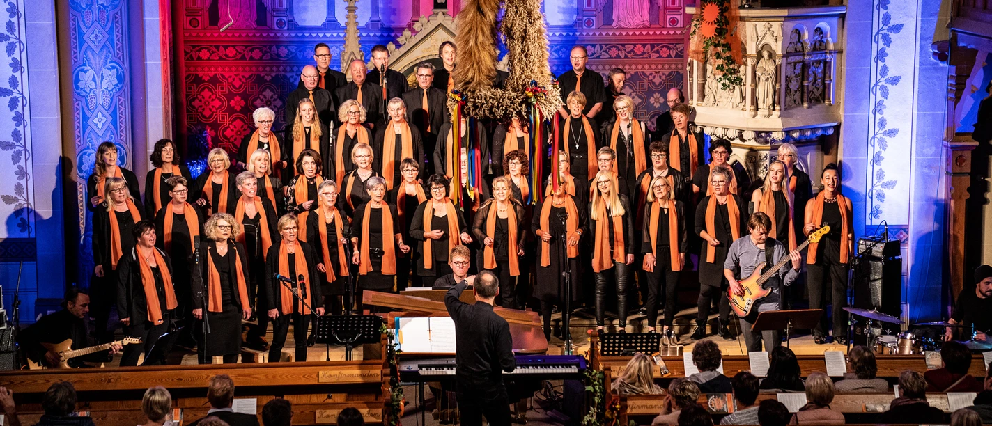 Joyful Gospels Gospelchor mit Dirigent und Band vor Altar, Publikum in Kirchenbänken